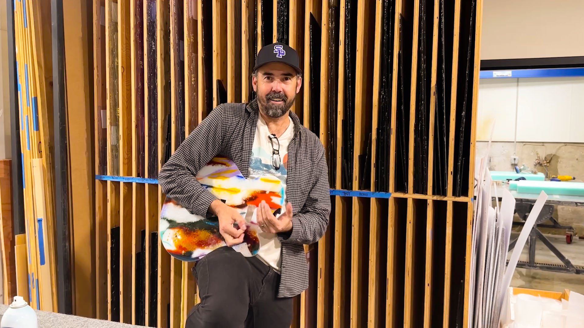Tim Carey holding a finished glass guitar inside the studio, pride and relief after the build