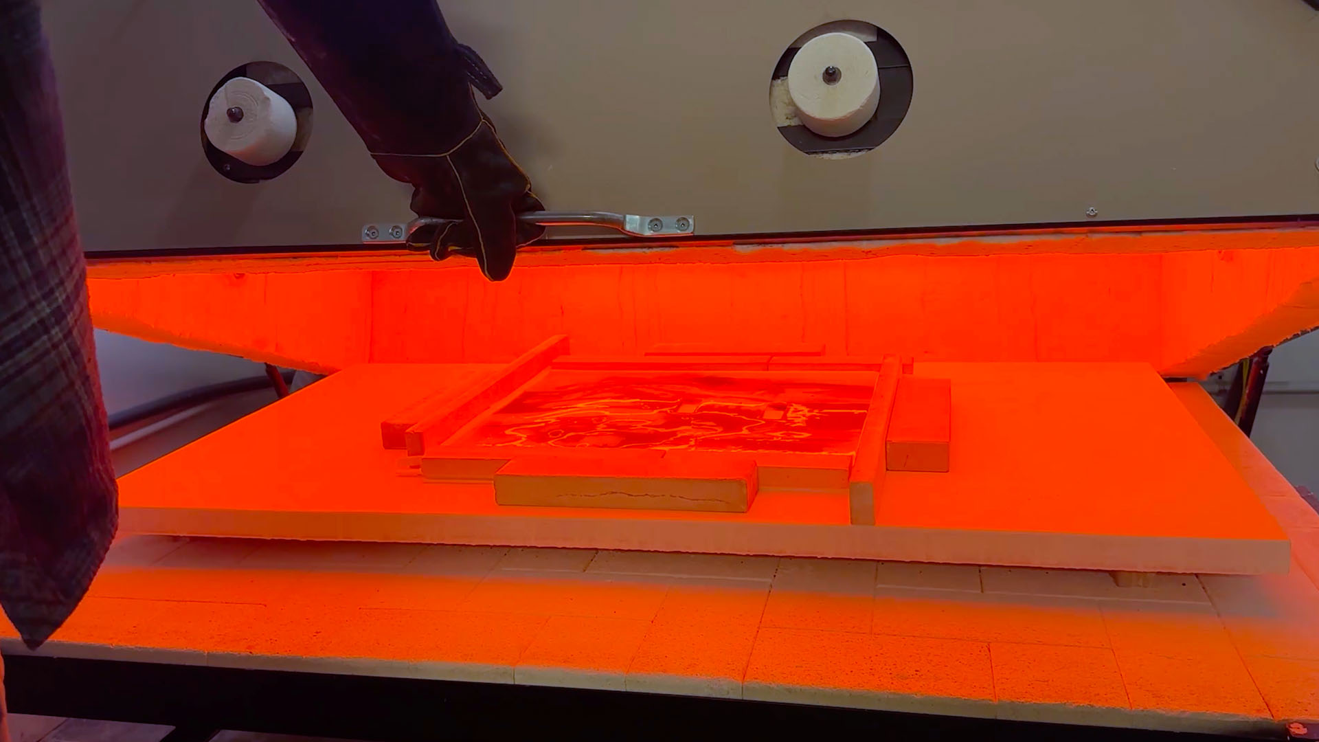 Glass pieces glowing inside a kiln during the firing process, tension at a critical stage